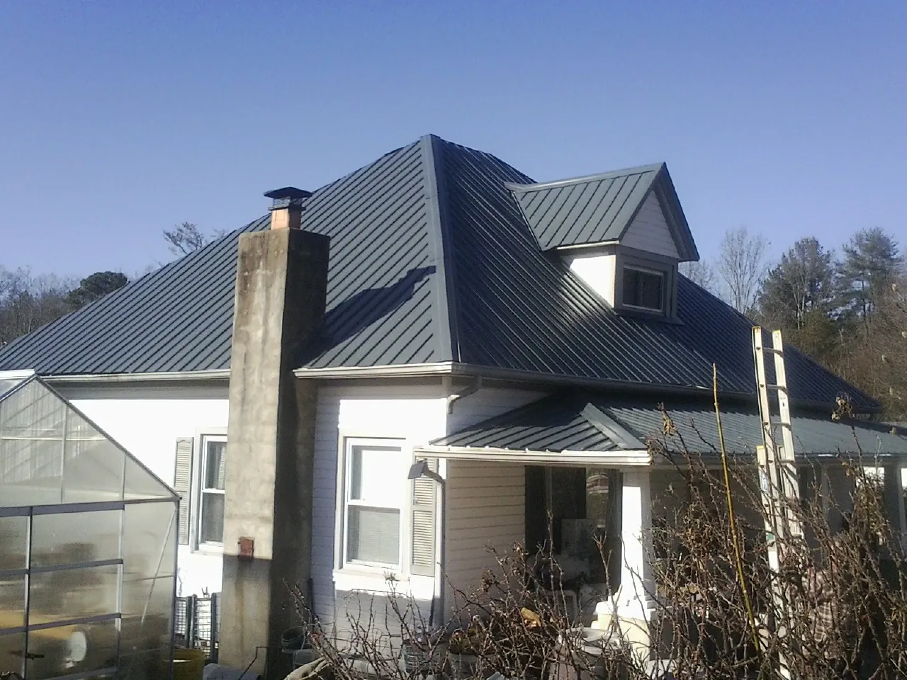 Dark blue standing seam metal roof on a white farmhouse with dormer — Slate & Tile Roof Repair by Roofing Brothers in Pendergrass