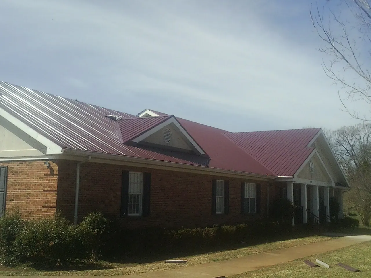 Red metal roof with gabled entries on a long brick building, from a Hail Damage Roof Repair job in Pendergrass