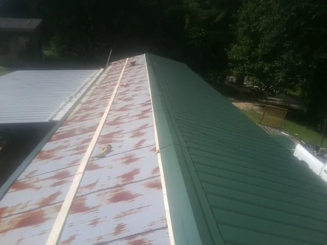 Old rusted panels beside newly installed green metal roofing — Wind Damage Roof Repair by Roofing Brothers in Pendergrass