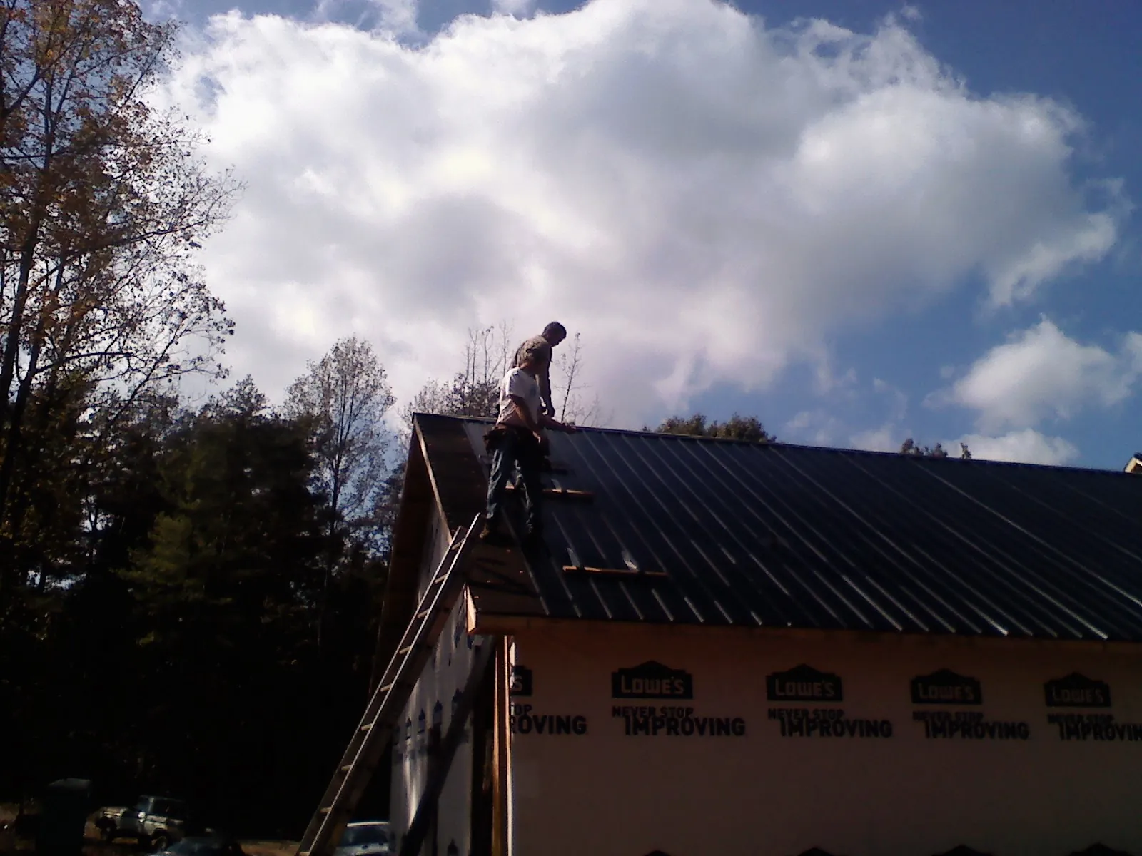 Roofer fastening dark metal panels high against a cloudy sky, from a Roof Inspection job in Pendergrass