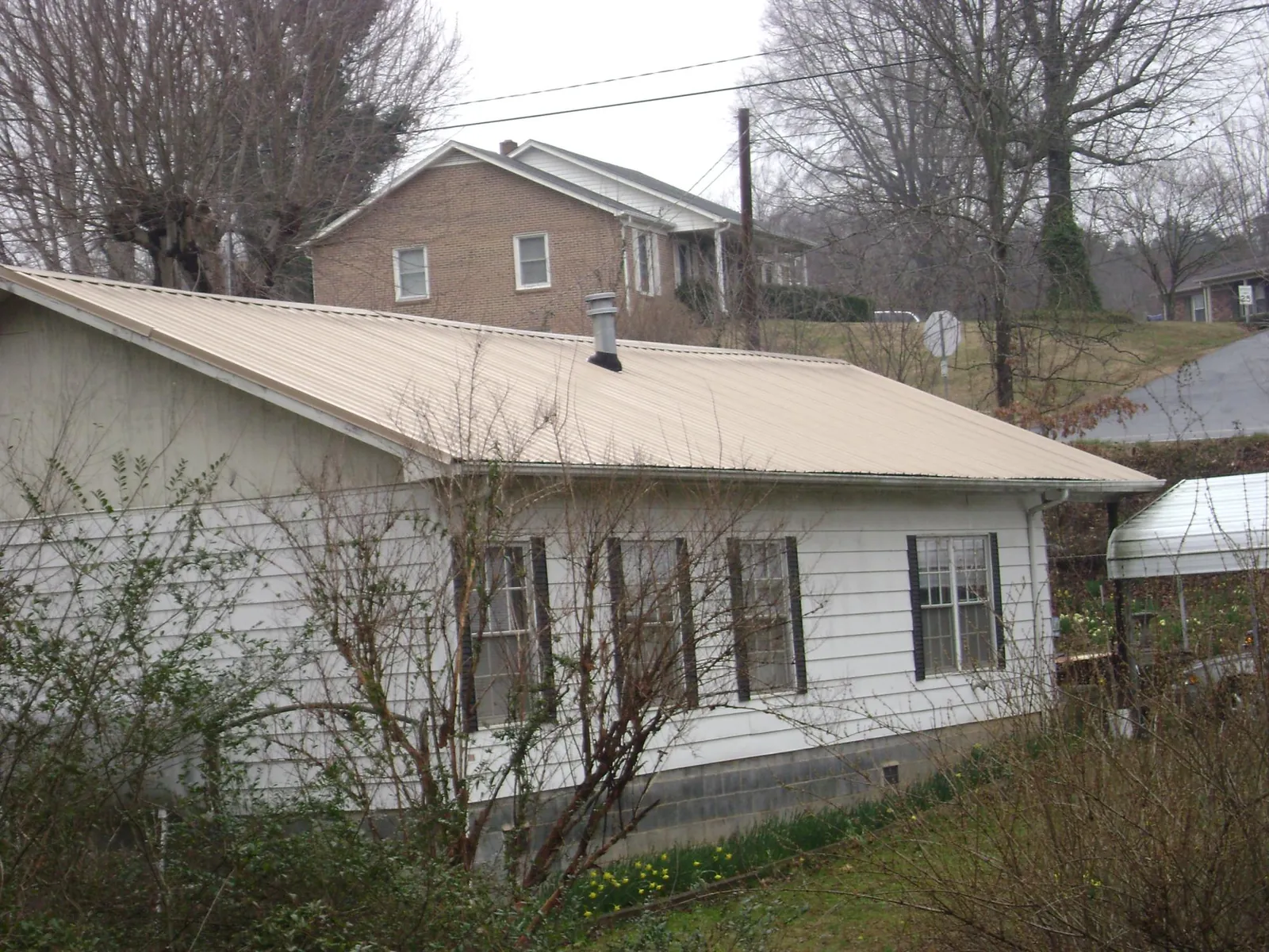 Tan metal roof on a white sided house set into a hillside — Commercial Roofing by Roofing Brothers in Pendergrass