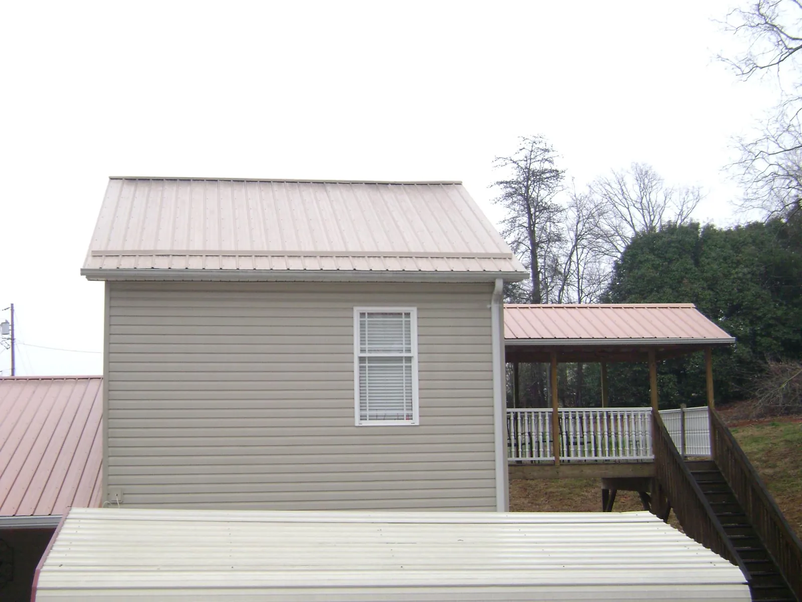 Tan metal roofs on a two story addition and attached porch, from a Roof Replacement job in Pendergrass